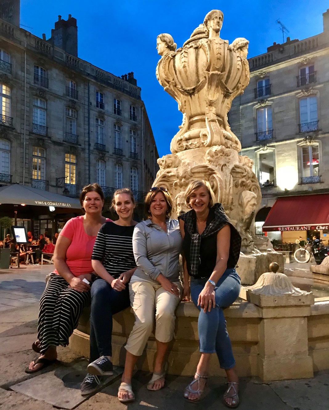 4 femmes assises sur le bord d'une fontaine