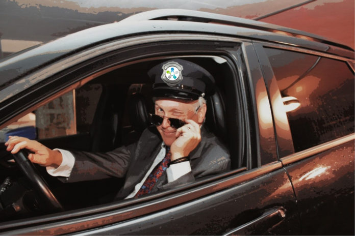 Dr Leduc déguisé en chauffeur de limousine, le logo d'Agrément sur sa casquette. Il a baissé ses lunettes de soleil et fait un clin d'oeil.