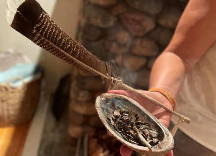 Main tenant une plume et un coquillage dans lequel brûle de la sauge sacrée