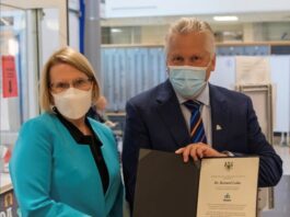 Une femme et un homme masqués sont côte à cote; l'homme tient un document officiel entre ses mains