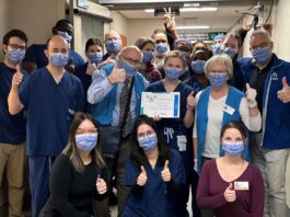 Groupe de membres du personnel hospitalier dans un corridor. Ils sont souriants malgré le port du masque et font tous le signe du pouce en l'air. la personne au milieu de l'image tient un certificat dans ses mains