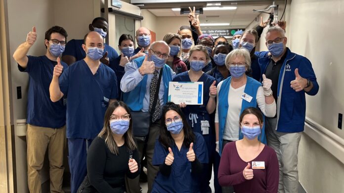 Groupe de membres du personnel hospitalier dans un corridor. Ils sont souriants malgré le port du masque et font tous le signe du pouce en l'air. la personne au milieu de l'image tient un certificat dans ses mains