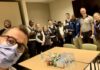 Le gestionnaire du programme de santé mentale fait un selfie dans une salle de réunion. Derrière lui, un groupe de membres de l'équipe au programme de santé mentale, accompagnés de membres de l'équipe de Sécurité. Des cannettes de boissons gazeuses et de jus sont sur une table.