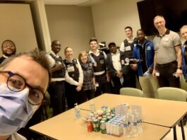 Le gestionnaire du programme de santé mentale fait un selfie dans une salle de réunion. Derrière lui, un groupe de membres de l'équipe au programme de santé mentale, accompagnés de membres de l'équipe de Sécurité. Des cannettes de boissons gazeuses et de jus sont sur une table.