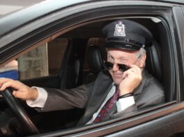 Dr Leduc déguisé en chauffeur de limousine, le logo d'Agrément sur sa casquette. Il a baissé ses lunettes de soleil et fait un clin d'oeil.
