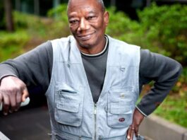 Grégoire Ahongbonon, vêtu d'une veste de jeans, appuyé contre la rampe d'un escalier extérieur