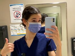Jeune femme masquée et portant des "scrubs" qui prend un selfie dans une salle de bain de Montfort avant son premier quart de travail