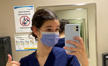 Jeune femme masquée et portant des "scrubs" qui prend un selfie dans une salle de bain de Montfort avant son premier quart de travail